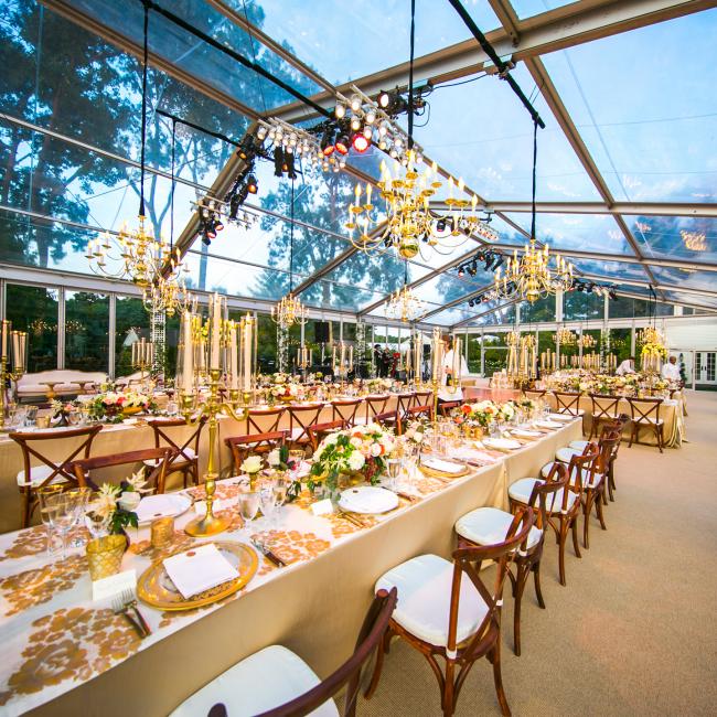 Beautiful place settings and chandeliers set up under a clear span tent.