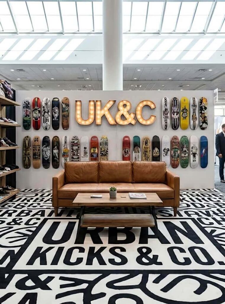 Stylish booth featuring a brown leather couch with a wooden table, surrounded by colorful skateboards and bold black-and-white text on the carpet.