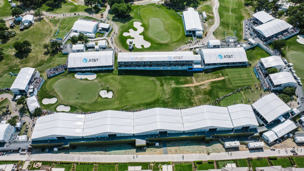Aerial view of a golf tournament featuring large white tents, green fairways, and spectators gathered near the greens and stands.