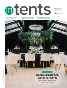 Elegant event space featuring round tables with black linens, lush green floral arrangements, and large windows, creating a sophisticated atmosphere.
