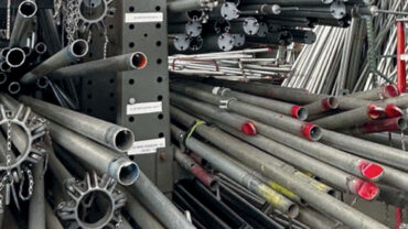 A cluttered warehouse filled with various steel pipes and metal structures, organized on shelves with a ladder in the foreground.