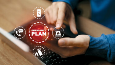 A person in a blue sweater using a laptop, interacting with emergency plan icons like SOS, fire, and phone symbols on the screen.