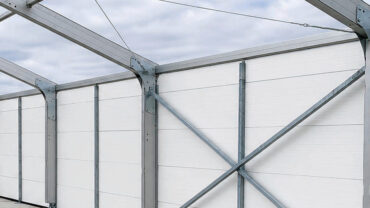 A large, partially constructed tent with a steel frame and white fabric walls, showing workers and an open sky in the background.