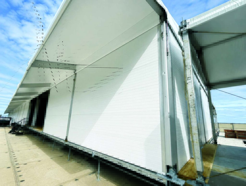 White insulated panels create a streamlined exterior of a large structure, set against a blue sky and reflecting modern architecture.