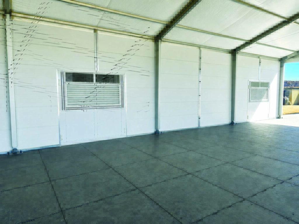 Interior of a large, empty space with white insulated walls and two vented windows, featuring a grey floor.